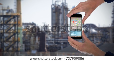 Cropped hands of businesswoman holding 3D mobile phone against image of factory