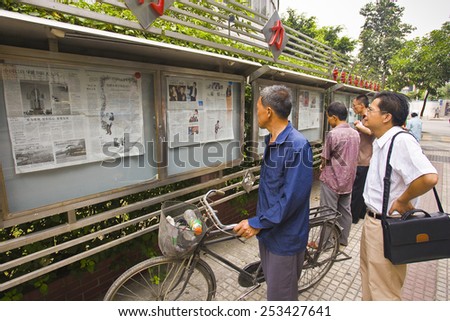 GUANGZHOU, GUANGDONG PROVINCE, CHINA - OCTOBER 13, 2006: Men reading newspapers posted in public display case on sidewalk, in the city of Guangzhou.