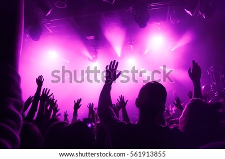 Raised hands of fans during a concert (show or performance) on the background of purple rays of light