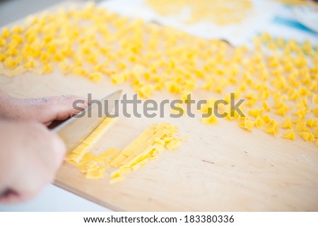 Woman hands cut home made pasta on a wooden cutting board.