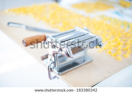 A traditional pasta machine on a wooden cutting board close to drying home-made pasta.