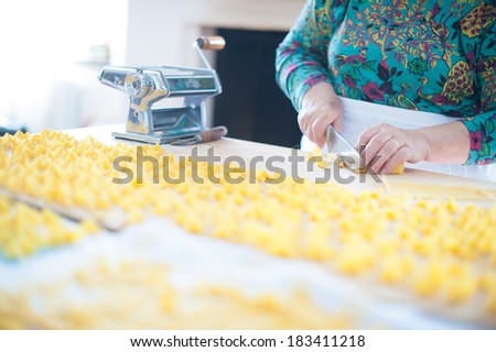 A beautiful traditional metal pasta machine on a wooden cutting board for drying pasta and woman\'s hands cutting a rolled up fresh pasta sheet.
