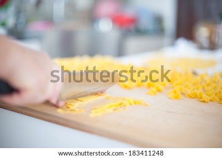 Woman\'s hand cuts with a knife in small squares a fresh pasta sheet.