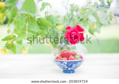 Front view of a cup with strawberries and a vase of flowers, in a shabby chic vintage mood.