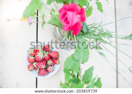 View from the top of a cup full of strawberries and a vase of flowers, in a shabby chic mood.