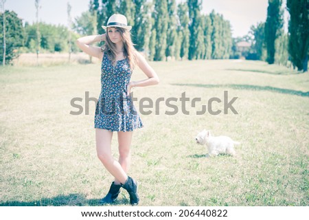 A beautiful blonde young woman enjoying spare time with her small dog in a park, with vintage-like effects.