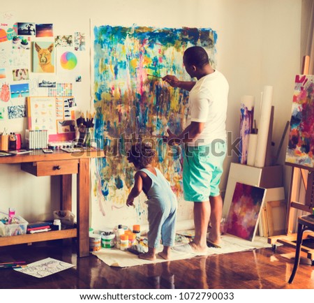 Black artist dad doing his art work with his child sitting nearby