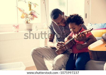African father teaching son how to play guitar