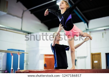 Coach training young gymnast to balance on a balance beam