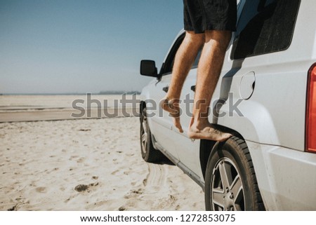 Man stepping on a wheel of his car at the beach