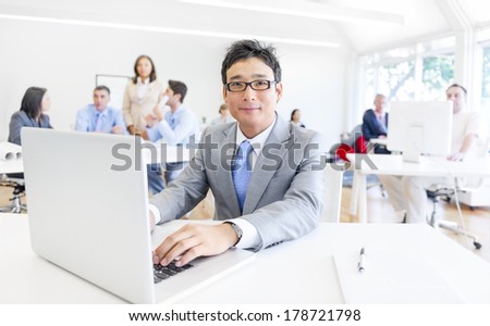 Asian Man Smiling While Working on Laptop in Office