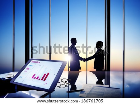 Silhouettes Of Two Businessmen Shaking Hands Together In A Board Room