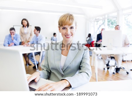 Caucasian business woman smiling at the camera while working on her laptop.