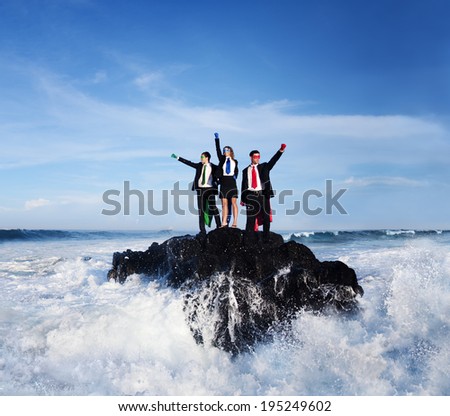 Three business people wearing superhero costumes posing on a rock with gushing waves.