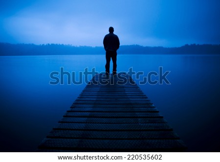 Man standing on a jetty by tranquil lake.