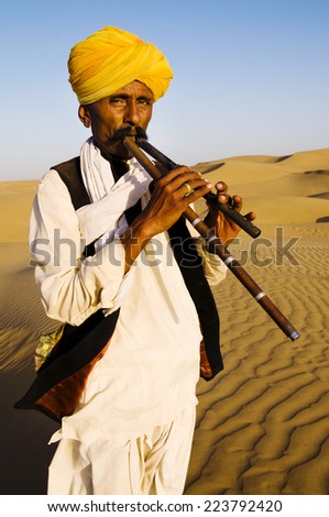 Indigenous Indian man playing wind pipe in a desert.