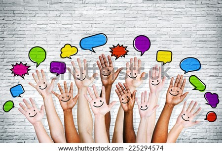 Multi ethnic people\'s hands raised with speech bubble by brick wall.