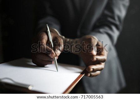 Closeup of hands cuffed forced to sign paper