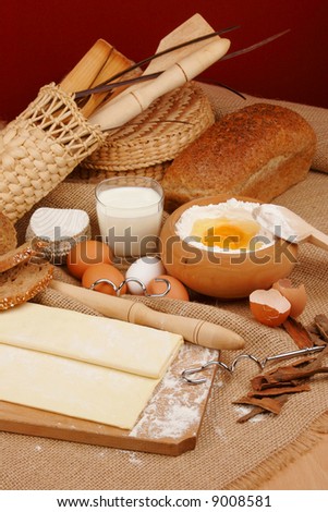 Rolling pin and dough for baking with scattered flour and a bowl of flour with eggs.