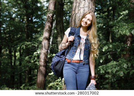 Young blonde girl hipster forest hike with a backpack in jeans