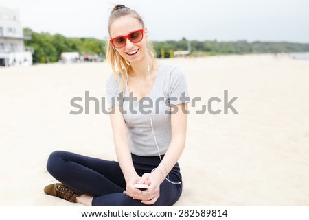 Sports girl on the beach wearing sunglasses listening music