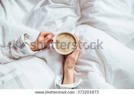 A cup of coffee in their hands in bed on a white blanket, simple, home, space in the frame