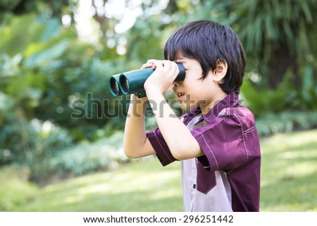 Little asian boy looking trough a binoculars with smiling face in park