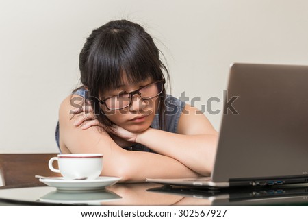 Asian Woman wearing glasses sitting on chair at home and fallen asleep while she works on a laptop
