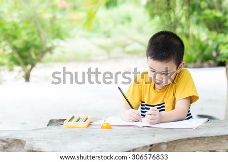 Little asian boy use pencil writing on notebook for writing book with smiling face on wooden table in the park