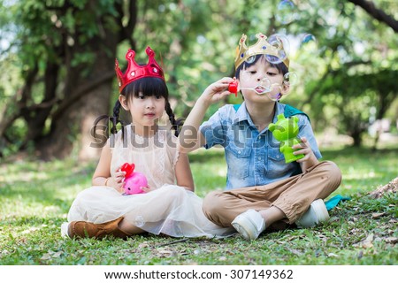 Asian little girl and boy as prince and princess is blowing a soap bubbles with smile face in park