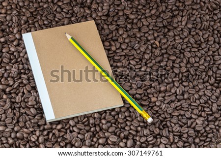 Paper notebook and pencil on roasted coffee seed background