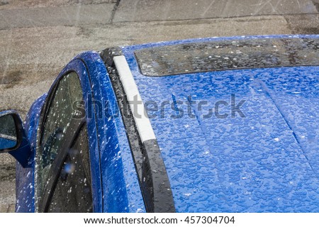 Hail falls on a blue car roof.
