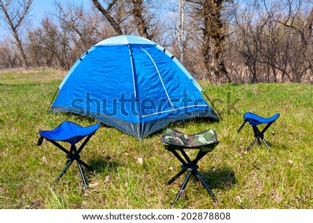 tourist camp with tent and chairs on spring meadow