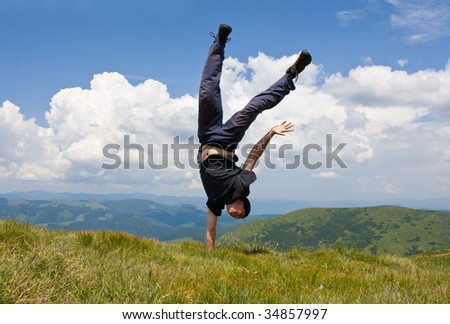 Happy man in mountains stay head over heels on one hand