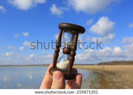 Hourglass in man hand on sky background