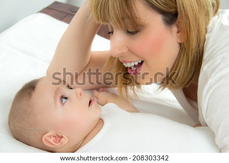 Mother leaning over her little baby boy at home and singing to him cheerfully