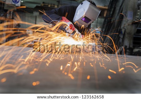 Metal wroker in a factory grinding with sparks Metal wroker in a factory grinding with sparks