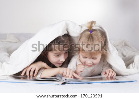 Two sisters reading bad time story in bad with white sheets