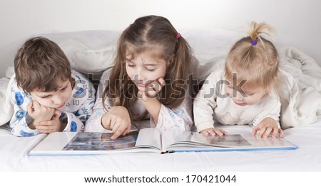 Three brothers boy and two girls lying in bed reading a book