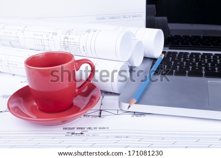 Architect blueprints with a silver laptop with pencil and red cup of coffee