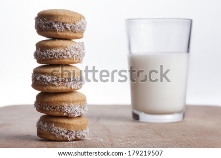 Coconut round cookies tower on wood plate with glass of milk in the background