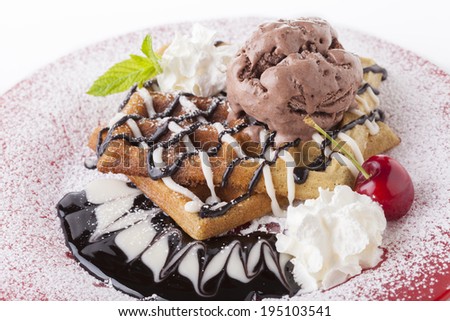 Belgian waffle with chocolate syrup whipped cream and chocolate ice cream with red cherry on red plate