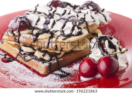 Belgian waffle with chocolate syrup whipped cream and    red cherry on red plate
