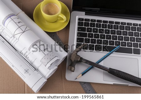 Architectural plans rolled with silver laptop hammer and a pencil