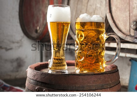 Two Beers with foam and old wood barrels in the background