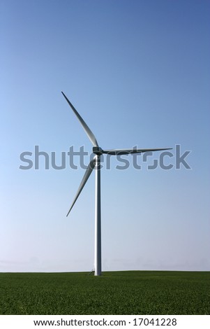 Electricity generating windmill in green field, against a clear blue sky
