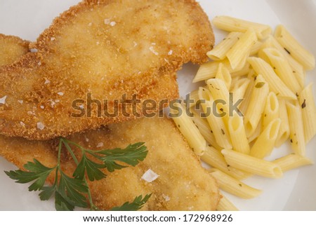 Breaded chicken fillet with pasta and parsley on white plate