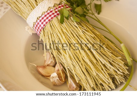 Fresh pasta (tagliolini) uncooked, tied with red and white band and rustic band, on wooden table.