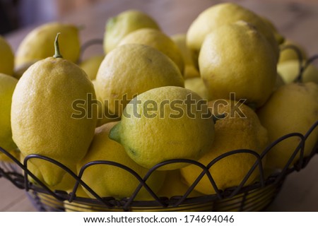 Group lemons freshly picked from the garden, on black iron fruit bowl on top of a wooden table
