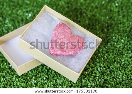 Pink heart in a small cardboard box, on green background with white polka dots